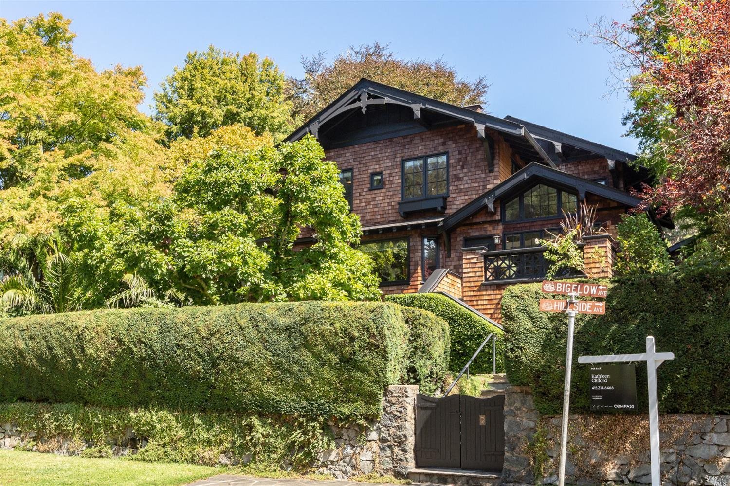 a view of a wooden house with a small yard and large trees