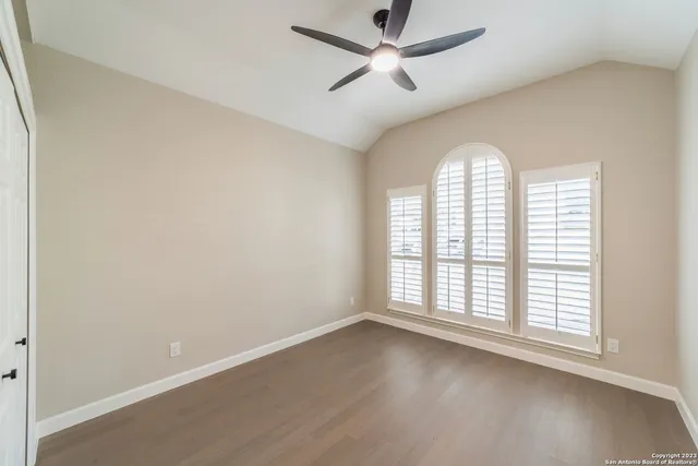 an empty room with wooden floor chandelier fan and windows