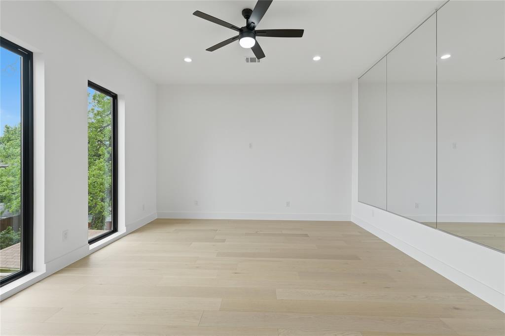 6038 Prospect Avenue Dallas, TX 75206 - Photo 38 of 40 Spacious room with light wood-finish flooring, two large vertical windows, a ceiling fan with integrated lighting, recessed lighting, and a mirrored accent wall