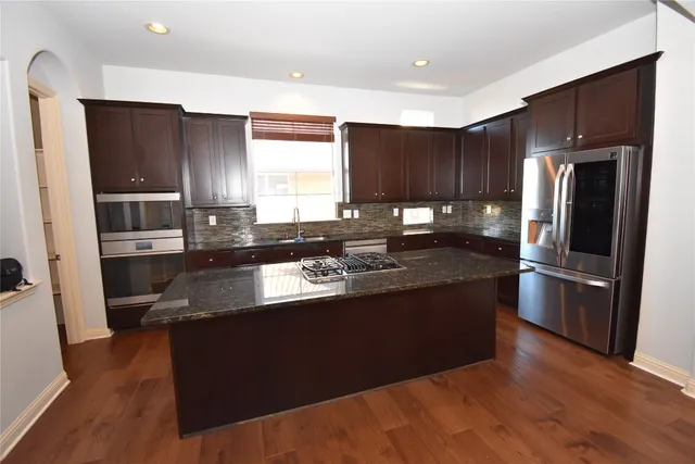 a kitchen with stainless steel appliances granite countertop a refrigerator a sink a stove a microwave and wooden floor