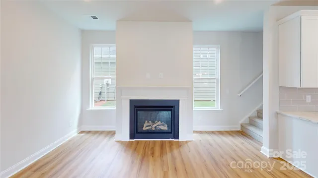 a view of an empty room with wooden floor fireplace and a window