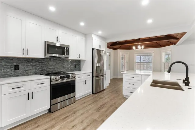 a kitchen with stainless steel appliances a stove a sink a refrigerator white cabinets and wooden floor