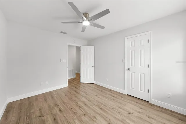 an empty room with wooden floor ceiling fan and windows