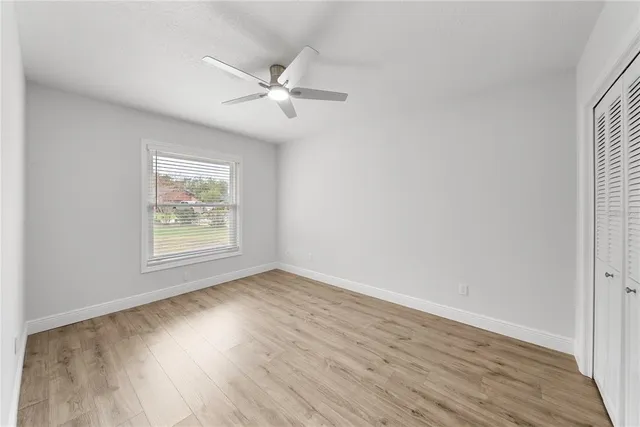 an empty room with wooden floor fan and windows