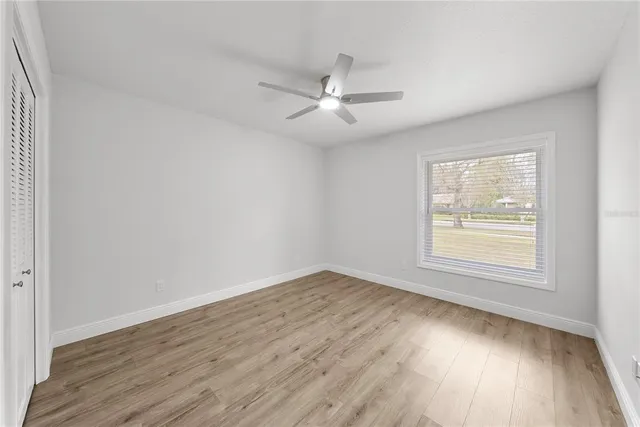 an empty room with wooden floor ceiling fan and windows