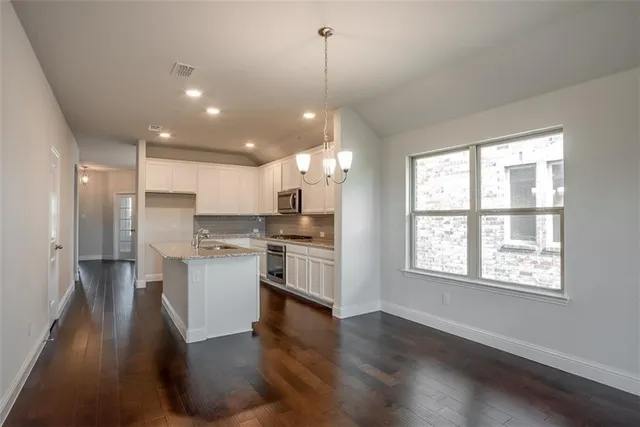 a kitchen with stainless steel appliances kitchen island granite countertop a refrigerator a sink dishwasher a stove and a dining table with wooden floor