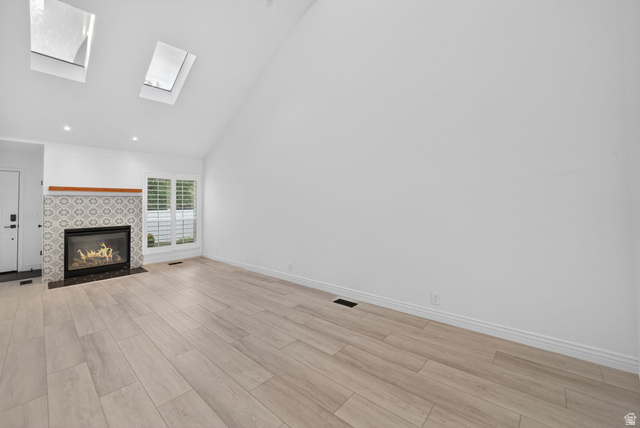 6969 South 855 East Midvale, UT 84047 - Photo 17 of 55 Vaulted ceiling space featuring two skylights, a fireplace with patterned tile surround and wood mantel, wood-finish flooring, and a window with plantation shutters