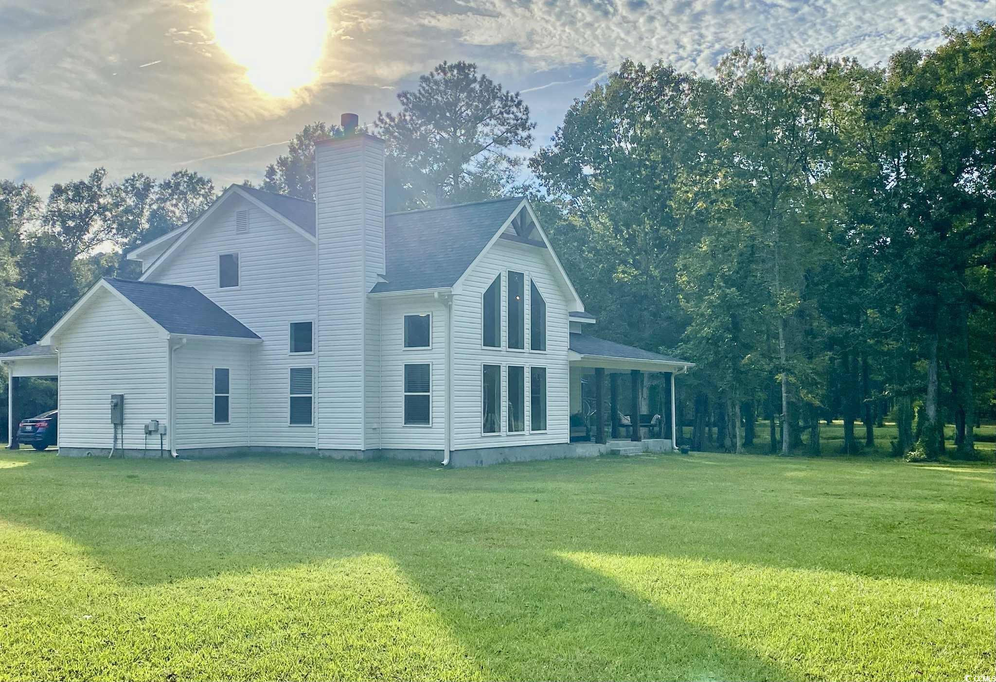 View of side of property featuring a porch, a lawn, and a chimney