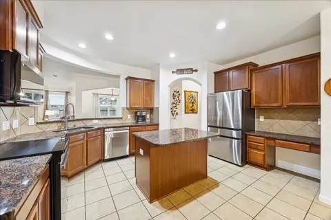 a kitchen with stainless steel appliances granite countertop a refrigerator a sink a stove top oven and a center island