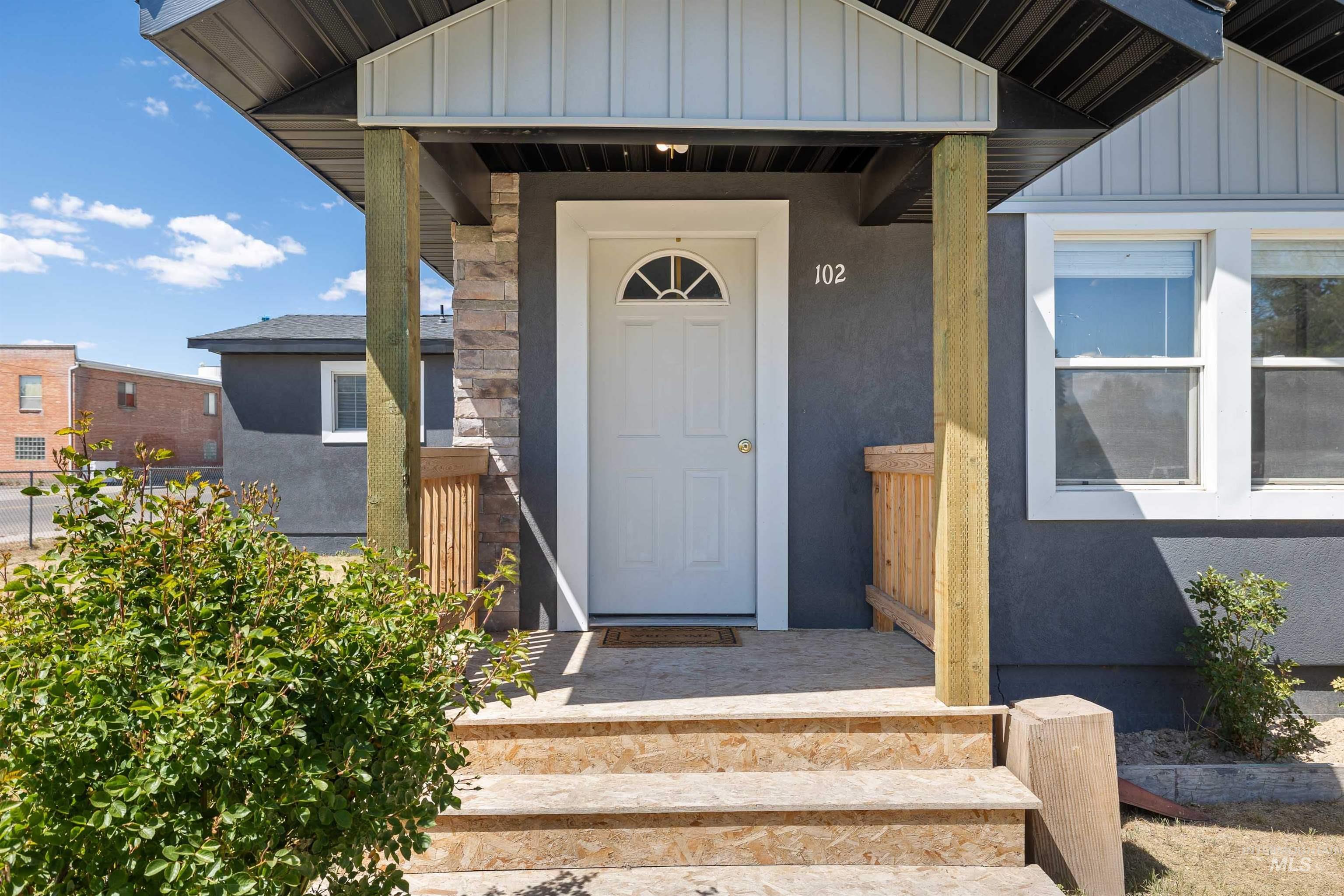 102 East 6th Street Rupert, ID 83350 - Photo 2 of 27 Front entry featuring a white panel door with an arched window, stone veneer accents, and a dark grey stucco exterior