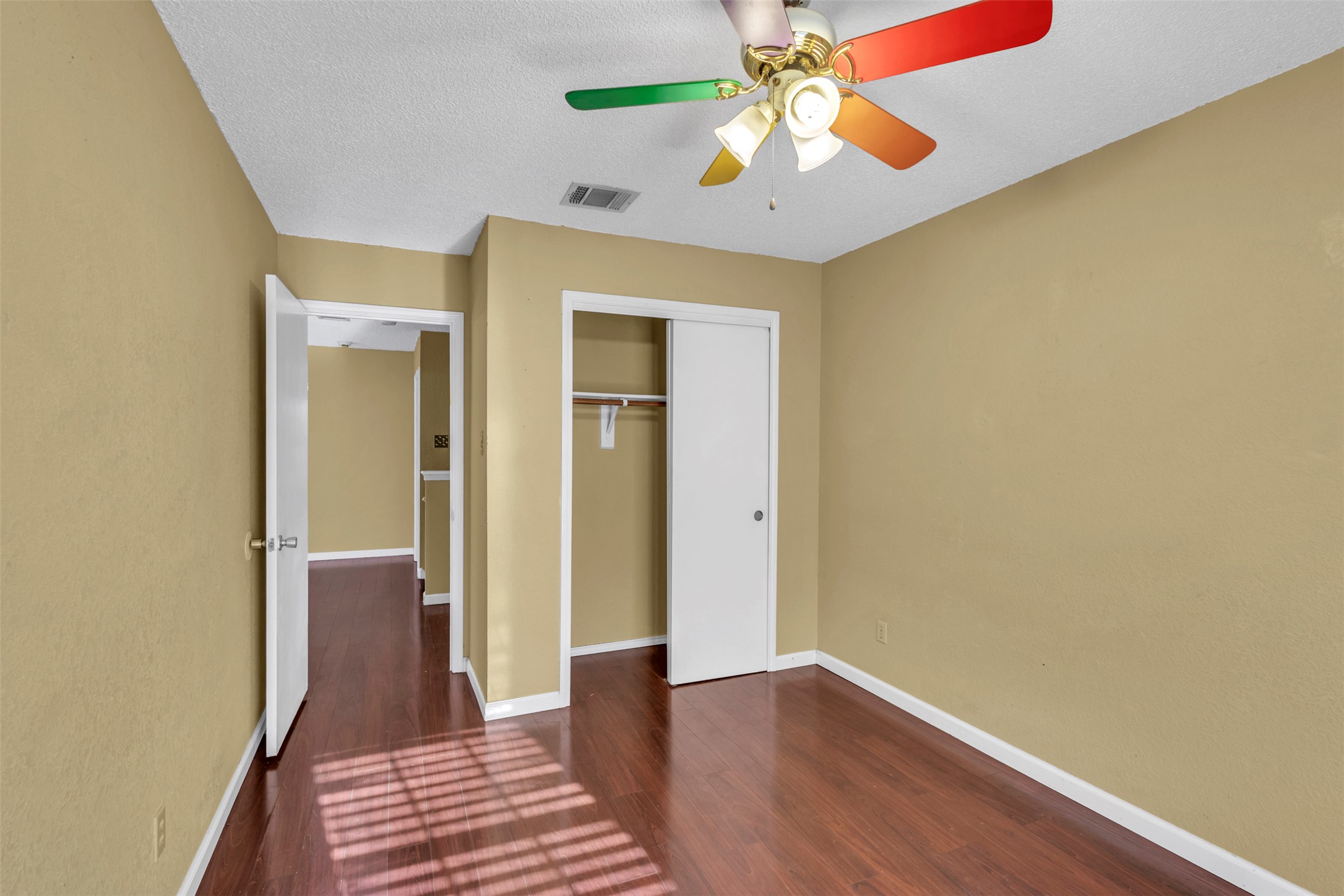 12922 Marimba Trail Austin, TX 78729 - Photo 18 of 28 Unfurnished bedroom featuring dark wood finished floors, a ceiling fan, a closet, and a textured ceiling