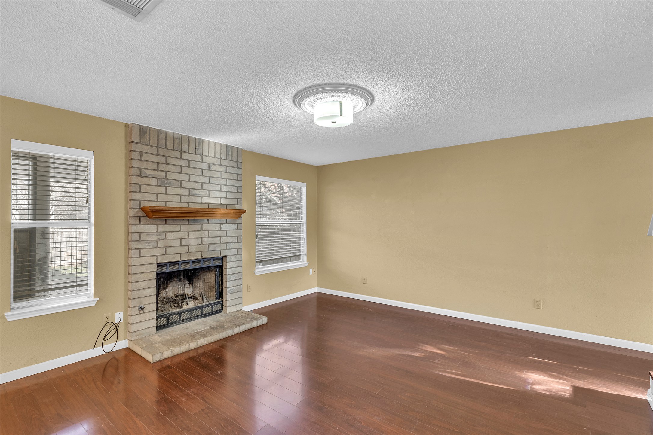12922 Marimba Trail Austin, TX 78729 - Photo 5 of 28 Unfurnished living room featuring a fireplace, dark wood-style floors, and a textured ceiling