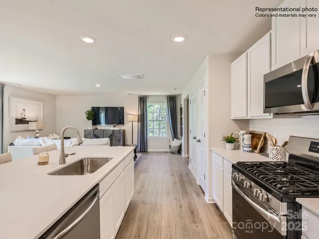 a kitchen with stainless steel appliances kitchen island granite countertop a stove a sink a refrigerator and white cabinets with wooden floor