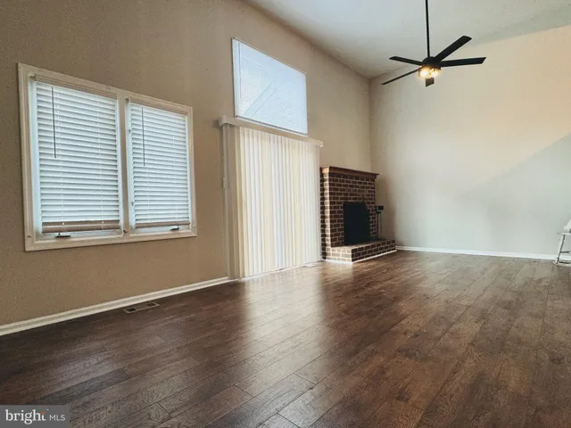 an empty room with wooden floor a ceiling fan and windows