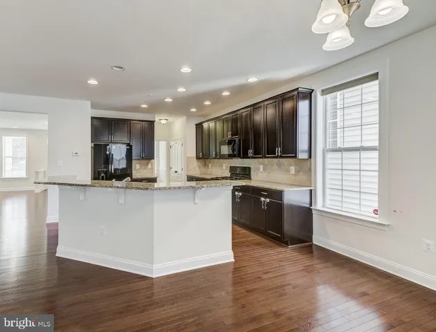 a large kitchen with stainless steel appliances granite countertop a stove a sink dishwasher a microwave oven and a refrigerator with wooden floor