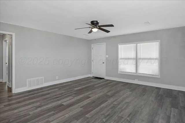 an empty room with wooden floor a ceiling fan and windows