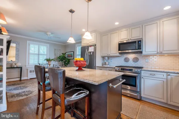 a kitchen with stainless steel appliances granite countertop a stove top oven a refrigerator a sink a dining table and chairs with wooden floor