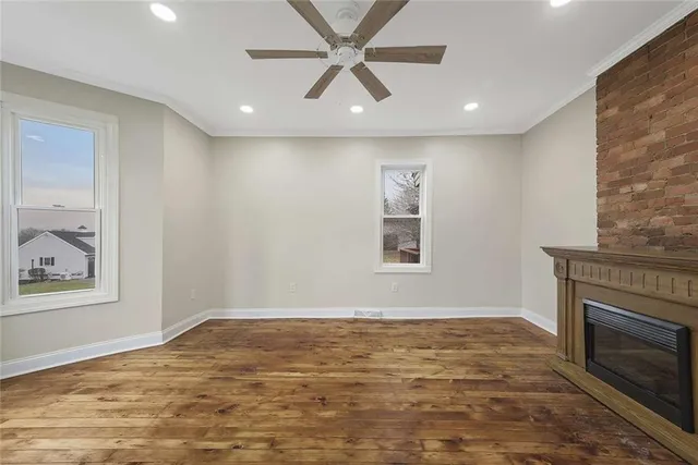 a view of a livingroom with a fireplace a ceiling fan and windows