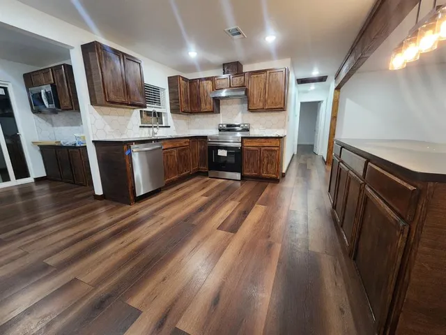 a kitchen with stainless steel appliances kitchen island granite countertop a stove a sink dishwasher a microwave oven and a refrigerator with wooden floor