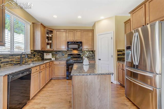 1415 Diamond Rim Drive Colorado Springs, CO 80921 - Photo 11 of 13 Kitchen with light wood-type flooring, a kitchen island, black appliances, stone countertops, and sink