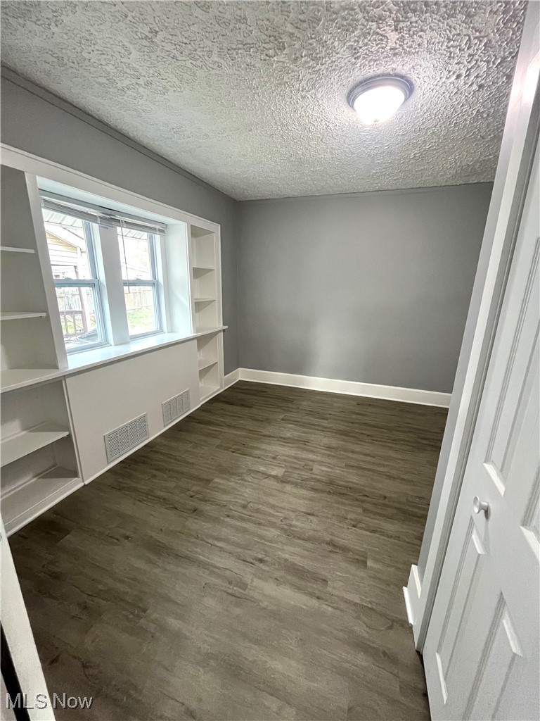 827 Inman Street Akron, OH 44306 - Photo 11 of 15 Empty room featuring dark wood-style floors, visible vents, baseboards, and a textured ceiling