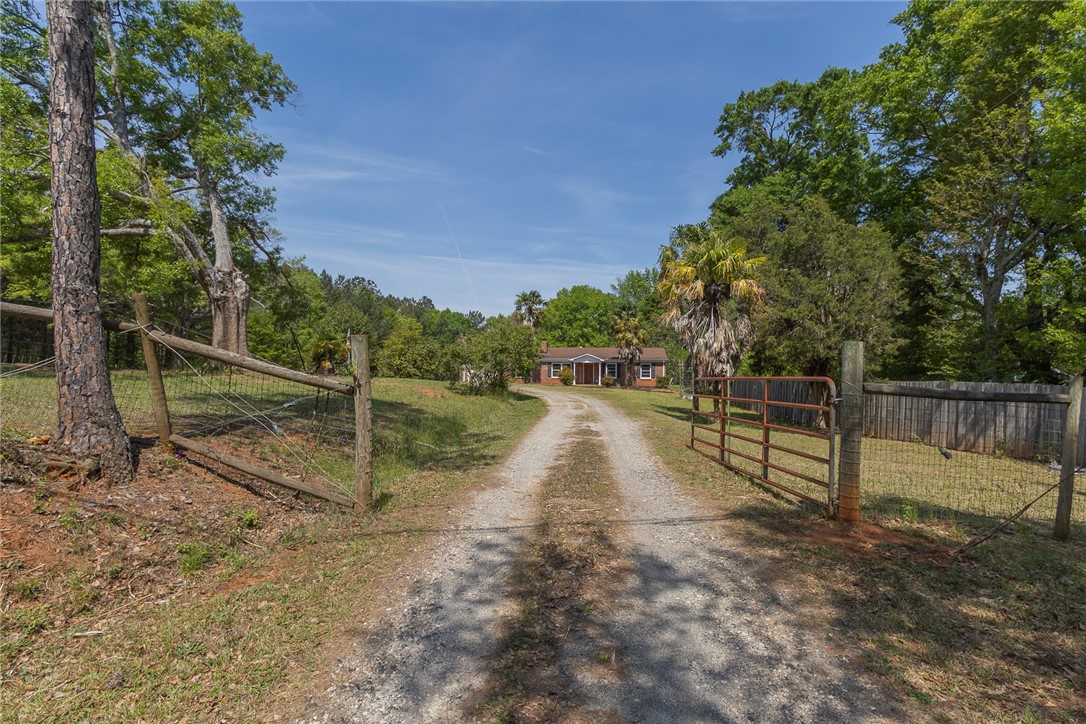820 Travis Road Anderson, SC 29626 - Photo 1 of 46 A long gravel driveway leads to a classic brick home nestled among lush trees and natural landscaping.