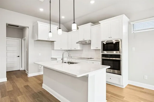 a kitchen with stainless steel appliances a stove a sink a center island and wooden floor