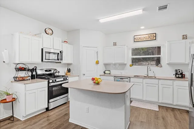 a kitchen with stainless steel appliances granite countertop a stove top oven a sink a refrigerator and white cabinets with wooden floor