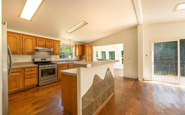 a kitchen with stainless steel appliances granite countertop a stove top oven a sink dishwasher a refrigerator and a microwave oven with wooden floor