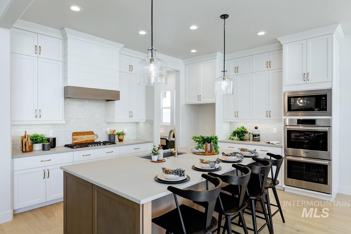 13265 North Spring Creek Way Boise, ID 83714 - Photo 4 of 35 Dual tone kitchen with a breakfast bar area, an island with sink, stainless steel appliances, light wood-type flooring, and pendant lighting