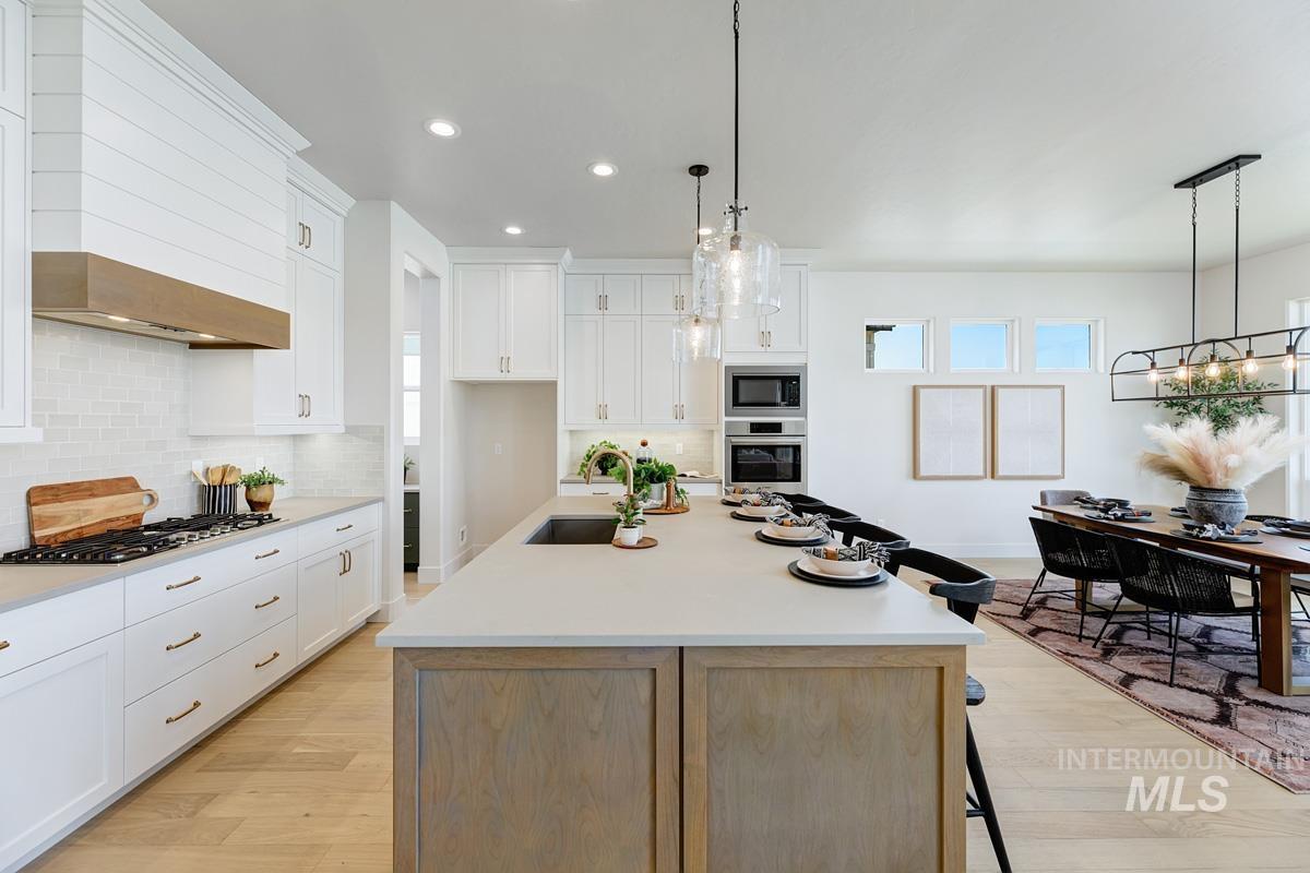 13265 North Spring Creek Way Boise, ID 83714 - Photo 9 of 35 Dual tone kitchen featuring a breakfast bar, a center island with sink, light wood-type flooring, stainless steel appliances, and two tone color scheme