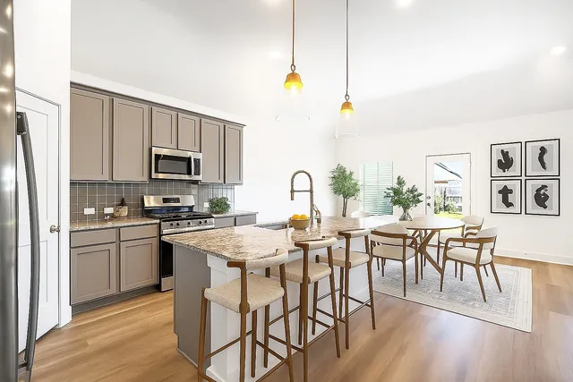 a kitchen with stainless steel appliances granite countertop a stove a refrigerator a kitchen island a dining table and chairs with wooden floor