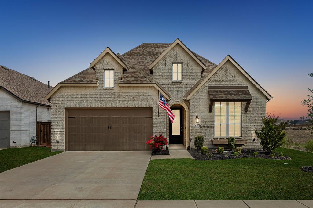 French country inspired facade with brick siding, a lawn, concrete driveway, and a shingled roof