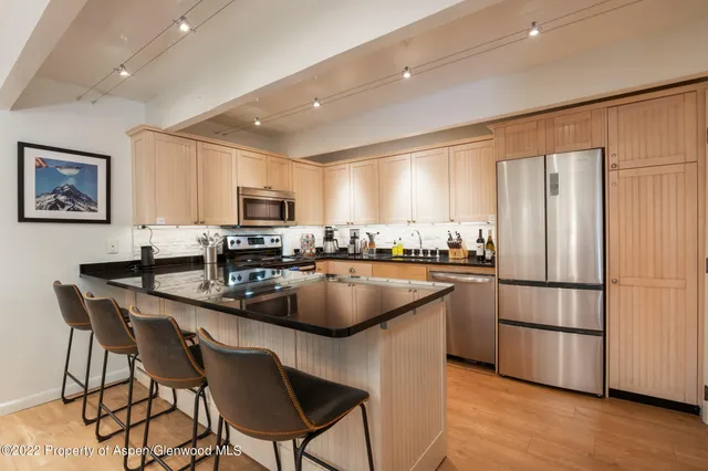 a kitchen with stainless steel appliances granite countertop a sink a stove a refrigerator a microwave a dining table and chairs with wooden floor