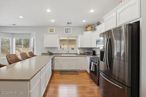 a kitchen with stainless steel appliances granite countertop a refrigerator a sink dishwasher a stove and white countertops with wooden floor