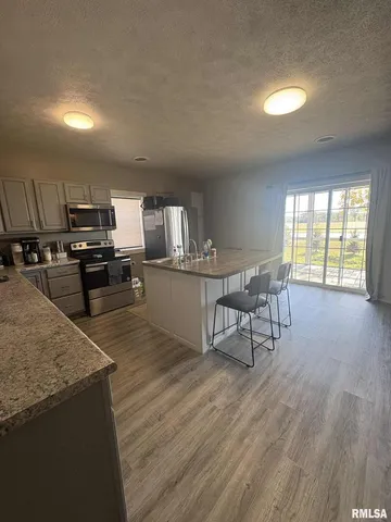 a kitchen with stainless steel appliances granite countertop a stove a refrigerator a sink a dining table and chairs with wooden floor