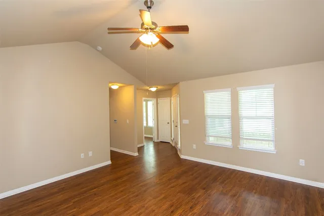 an empty room with wooden floor fan and windows