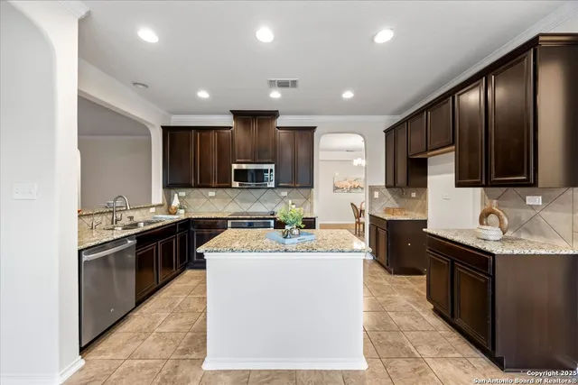 a kitchen with stainless steel appliances granite countertop a stove top oven a sink dishwasher a refrigerator and a microwave with wooden cabinets