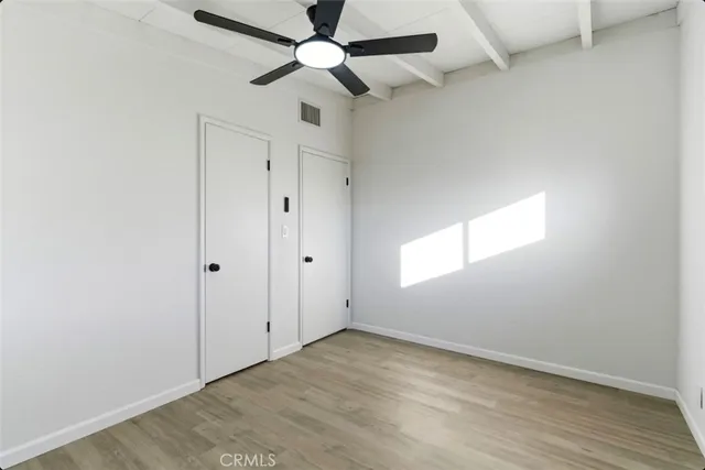 an empty room with wooden floor ceiling fan and windows