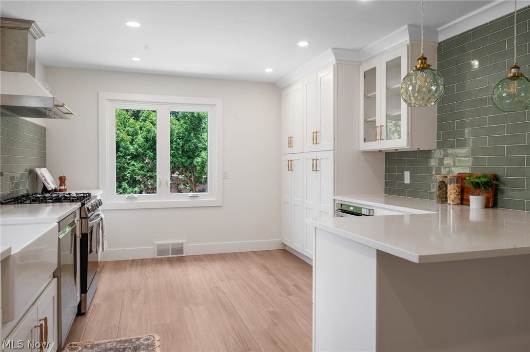 22625 Rye Road Shaker Heights, OH 44122 - Photo 11 of 38 Contemporary kitchen featuring light wood-finish flooring, white cabinetry with gold-tone hardware, a light gray countertop, and a green subway tile backsplash