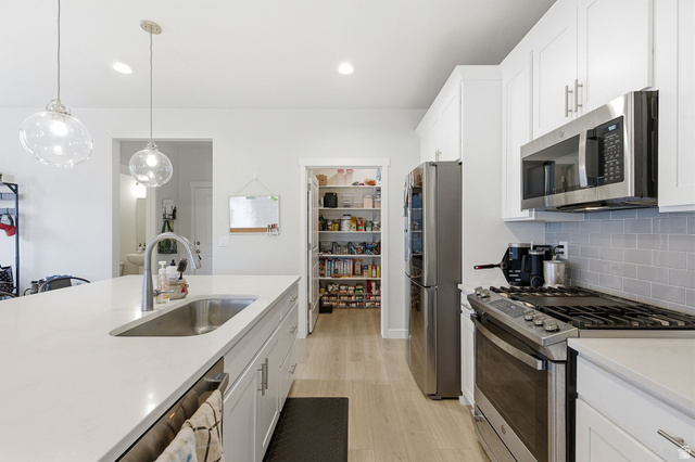 1038 South Old Towne Road Layton, UT 84041 - Photo 7 of 39 Bright kitchen featuring a large island with an undermount sink, quartz countertops, white cabinetry with contemporary hardware, stainless steel appliances, and a spacious pantry with shelving