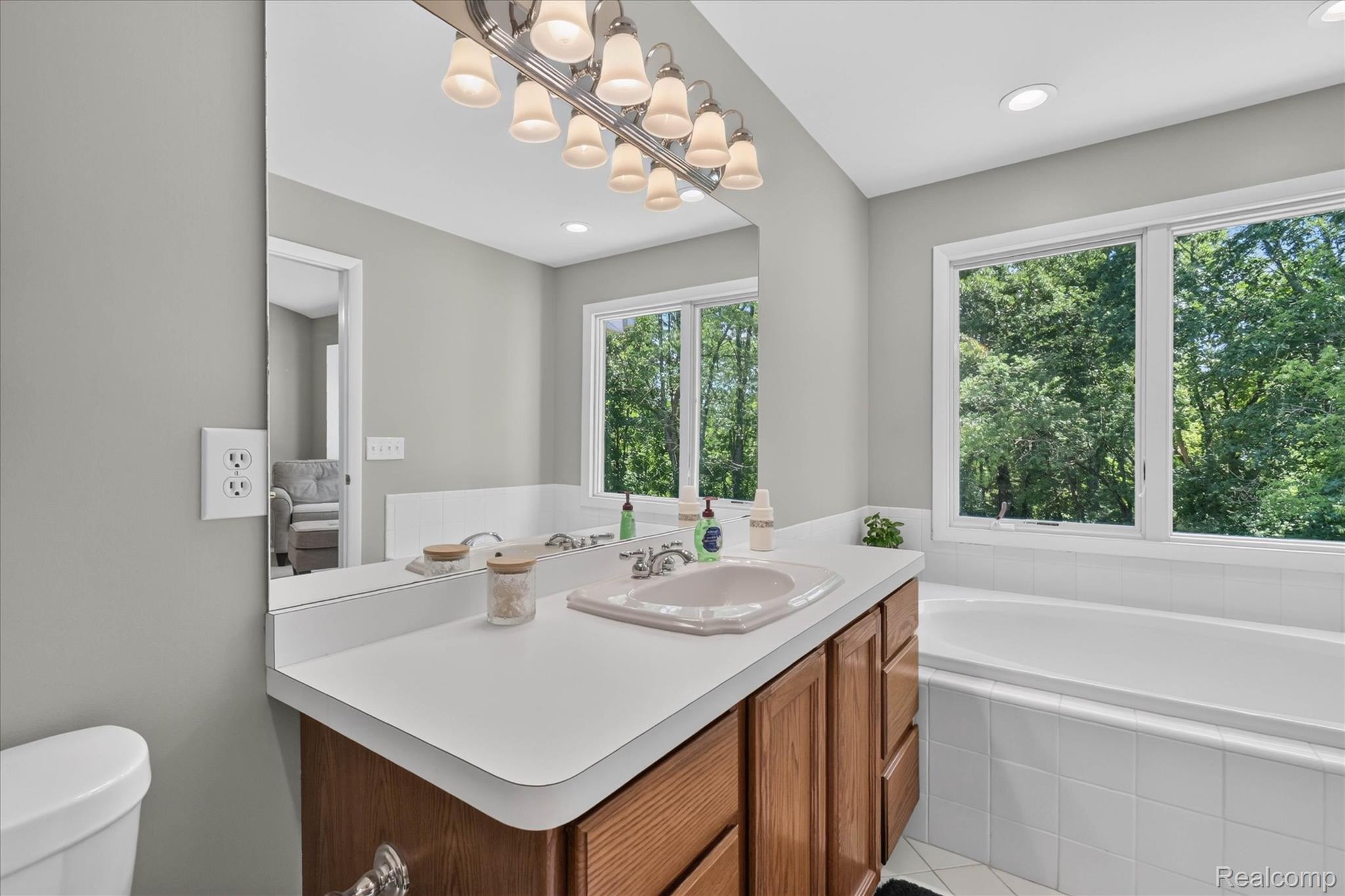 4037 Chilson Road Howell, MI 48843 - Photo 30 of 69 Bathroom featuring a single vanity with wood-finish cabinetry, a large integrated bathtub, and multiple windows providing natural light