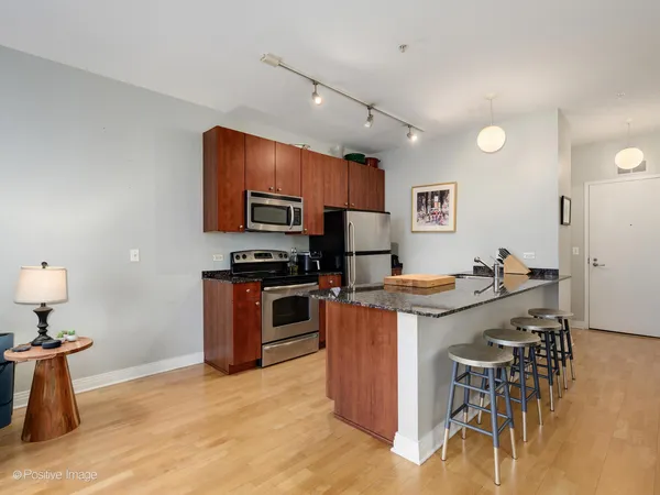 a kitchen with stainless steel appliances granite countertop a stove top oven a sink a dining table and chairs with wooden floor