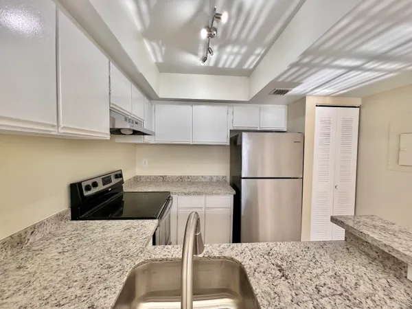 a kitchen with stainless steel appliances granite countertop a refrigerator a sink a stove a dining table and chairs with wooden floor