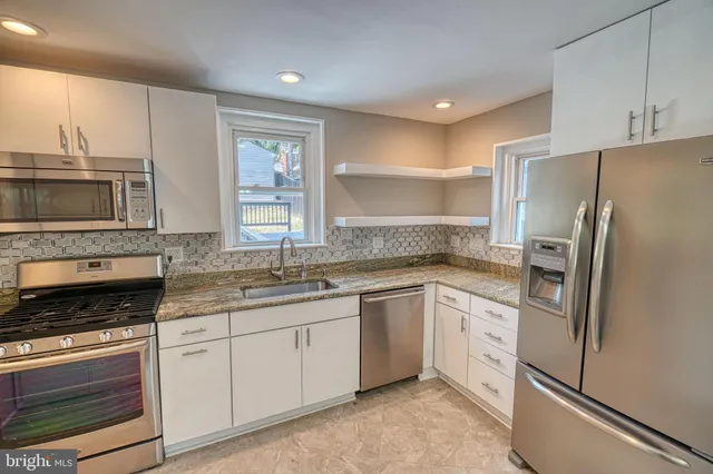 a kitchen with granite countertop a sink stainless steel appliances wooden floor and a window
