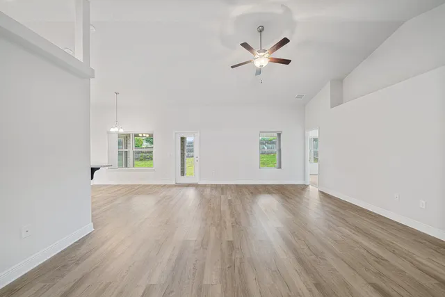 an empty room with wooden floor chandelier fan and windows