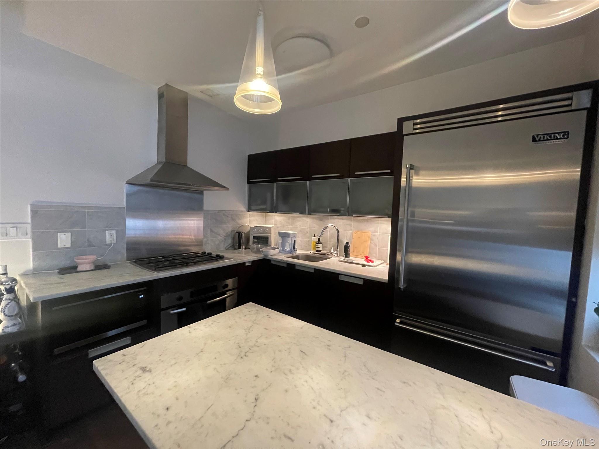 119 Fulton Street, Unit 5B Manhattan, NY 10038 - Photo 7 of 15 Kitchen featuring wall chimney exhaust hood, dark cabinets, a sink, stainless steel appliances, and backsplash