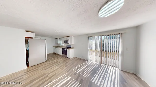 an empty room with wooden floor kitchen view and a window