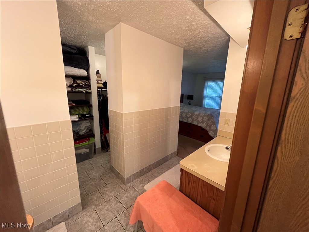 1455 Welch Road Painesville, OH 44077 - Photo 30 of 42 Ensuite bathroom featuring vanity, wainscoting, tile walls, a spacious closet, and a textured ceiling