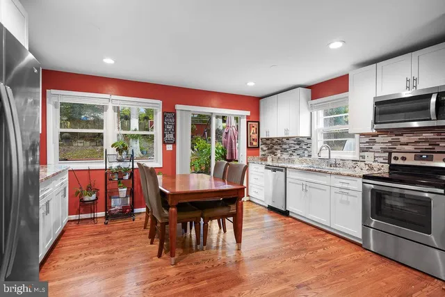 a kitchen with stainless steel appliances granite countertop a stove top oven a sink dishwasher a dining table and chairs with wooden floor